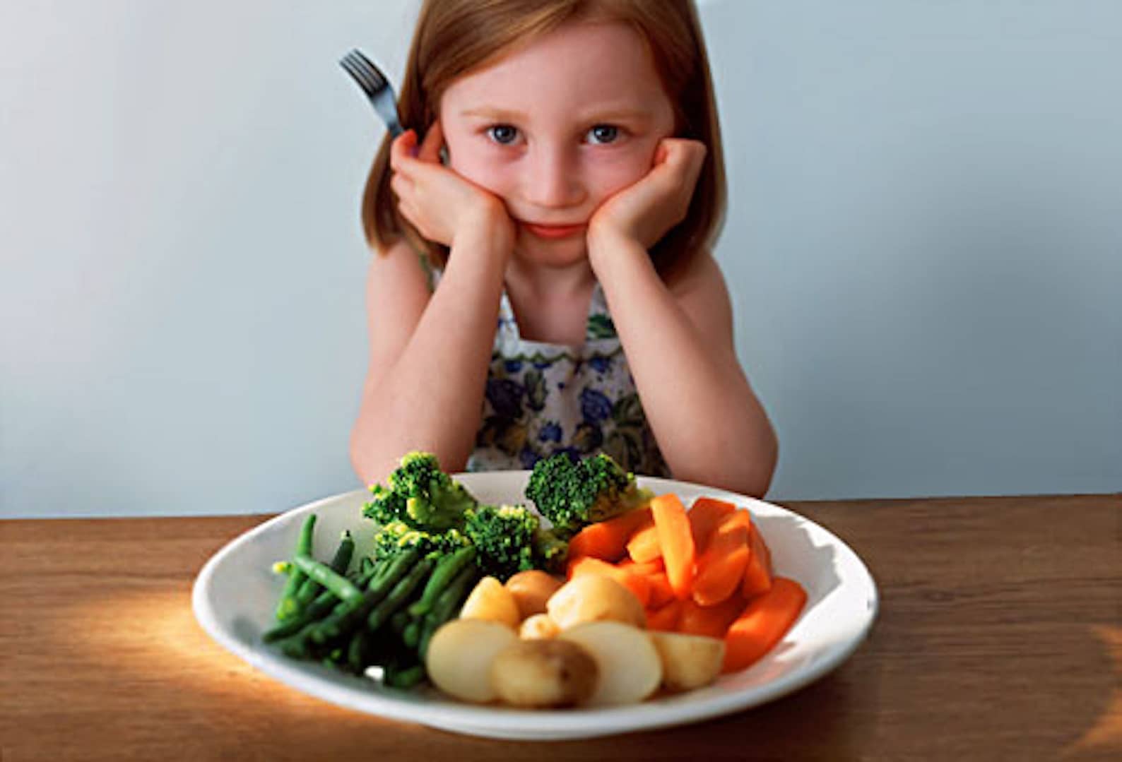 Little girl hesitant in front of a vegetables plate